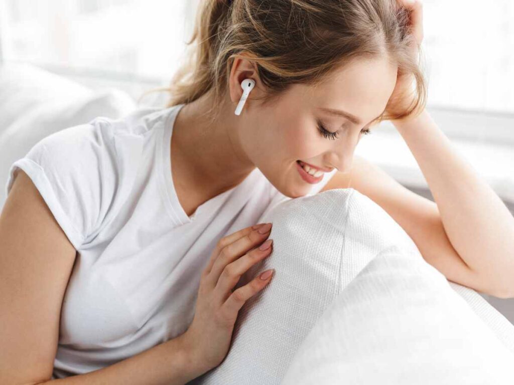 a lady wearing bluetooth earbuds and sitting on sofa